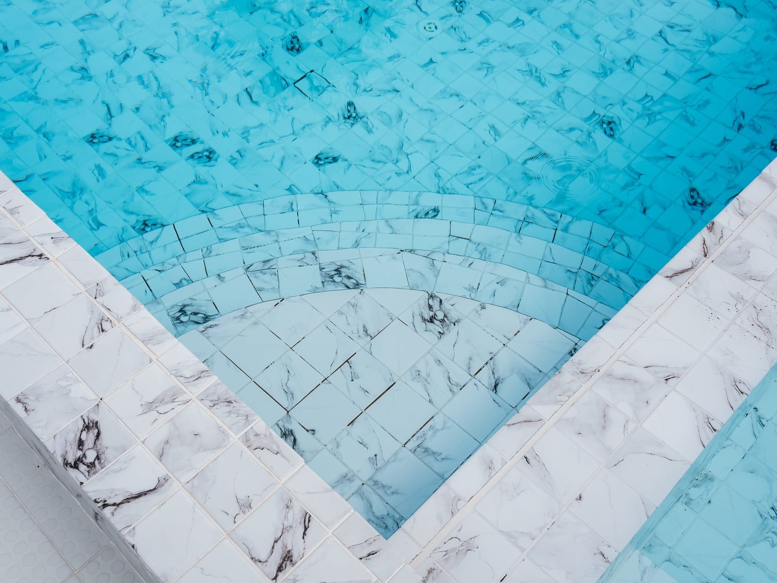 Tiled swimming pool steps seen through clear blue water with marble-pattern edges