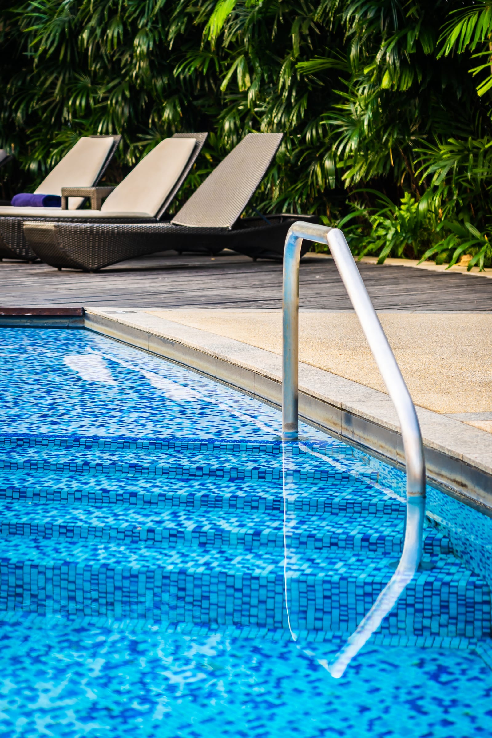A deck chair and umbrella beside an outdoor swimming pool in summer